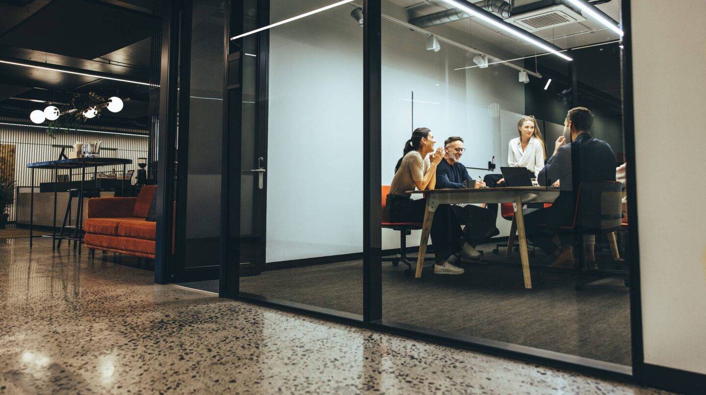 Business colleagues having a meeting in a transparent boardroom. Group of happy business professionals having a discussion during a briefing. Diverse businesspeople collaborating on a new project.