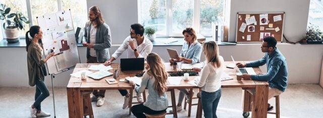 A group of diverse colleagues in an office setting watching a presentation