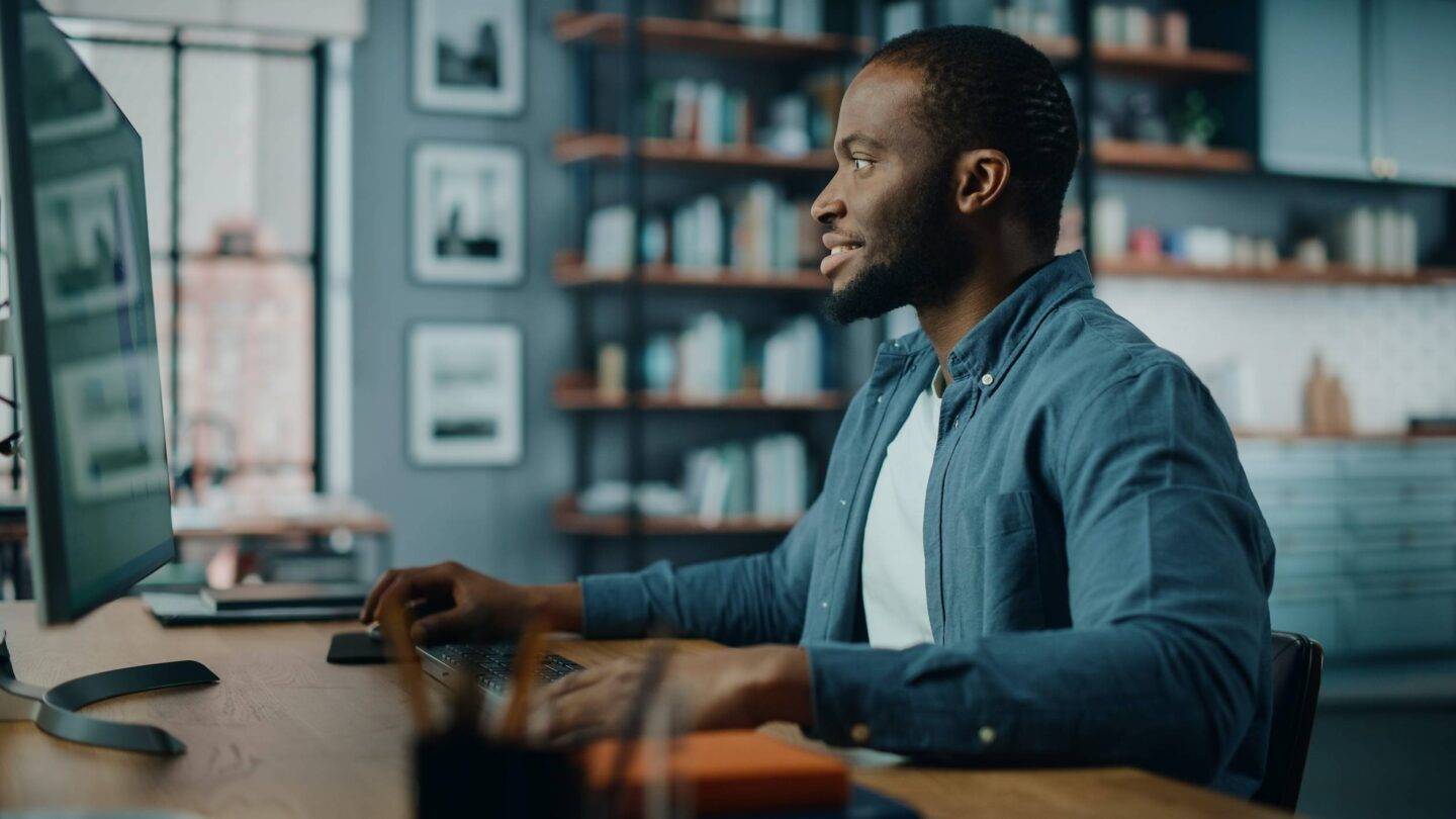 Handsome Black African American Specialist Working on Desktop Computer in Creative Home Living Room. Freelance Male is Working on a Finance Presentation Report for Clients and Employer.