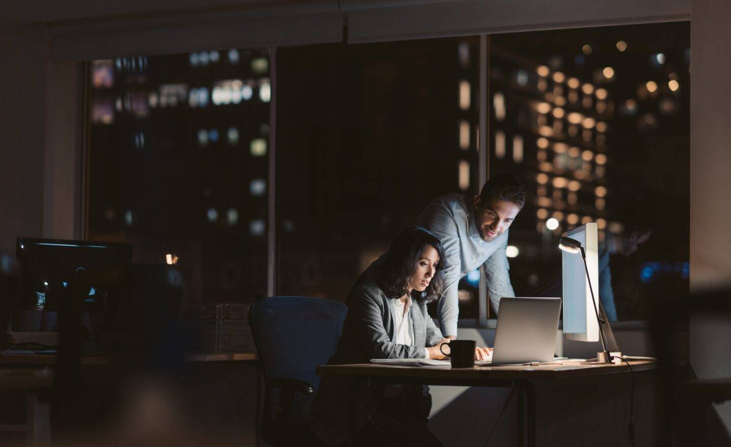 A man and woman at a work desk at night